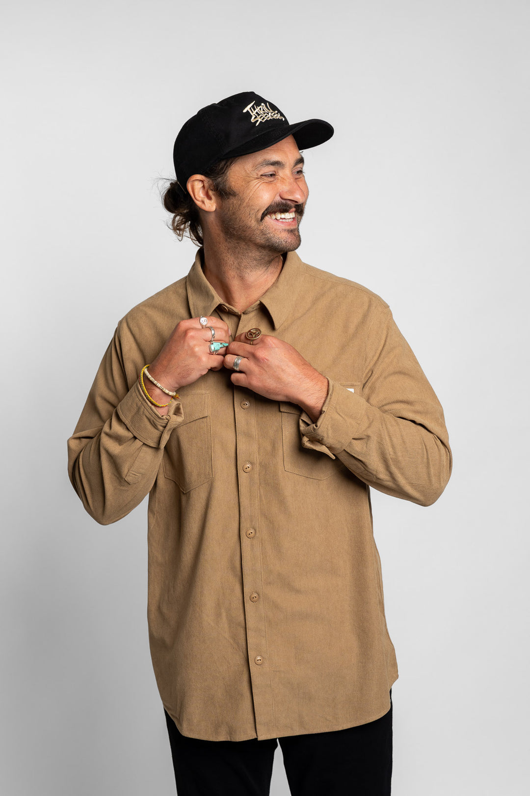 Man wearing a khaki button up long sleeve and black cap on a white background