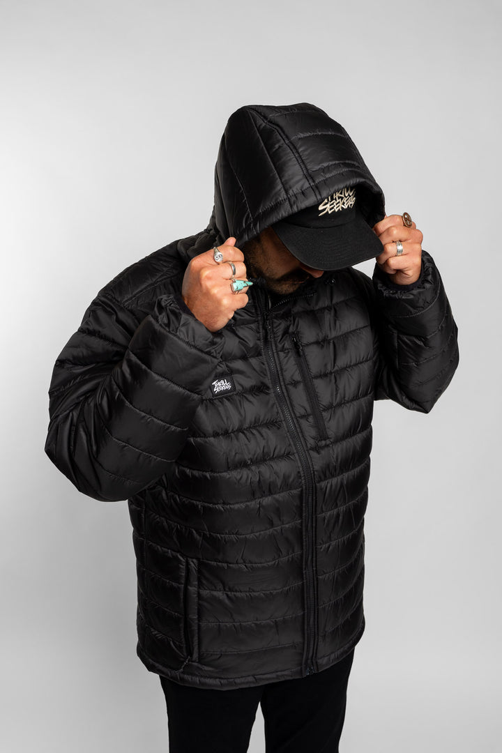 Person wearing a black quilted hooded jacket and cap on a white background