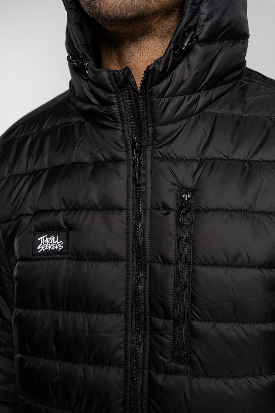 Close-up of a black puffer jacket with a Thrill Seekers logo on a white background