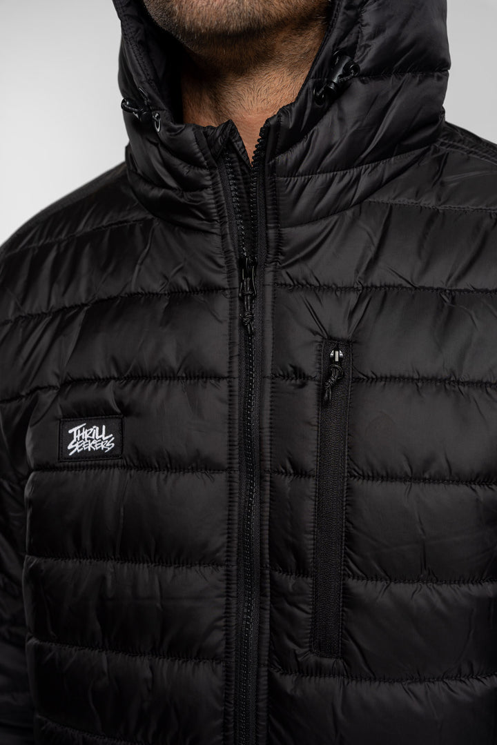 Close-up of a black puffer jacket with a Thrill Seekers logo on a white background