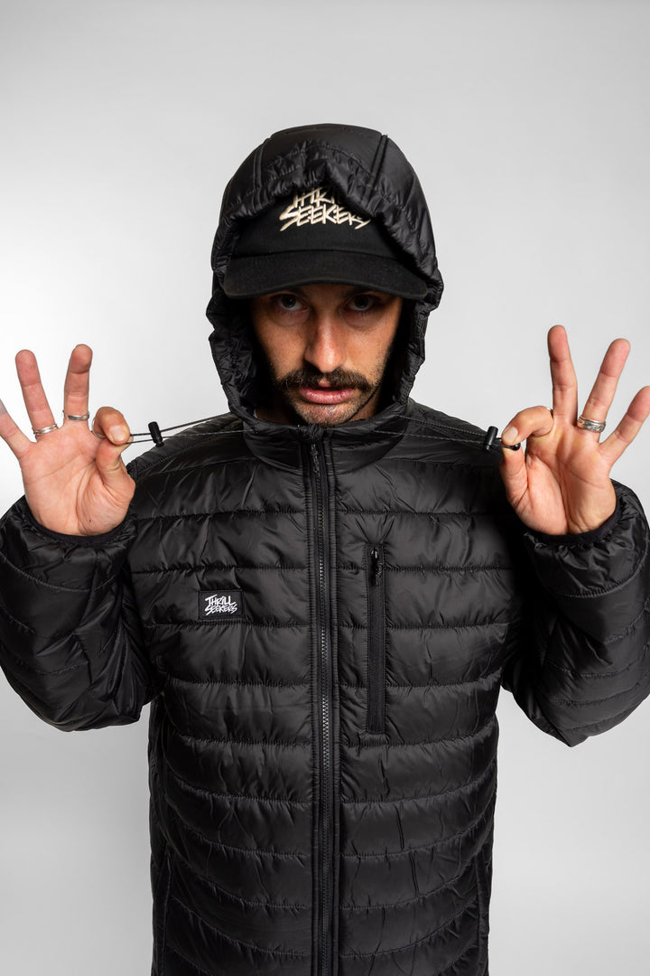 Person wearing a black puffer jacket and cap with Thrill Seekers logo on a white background