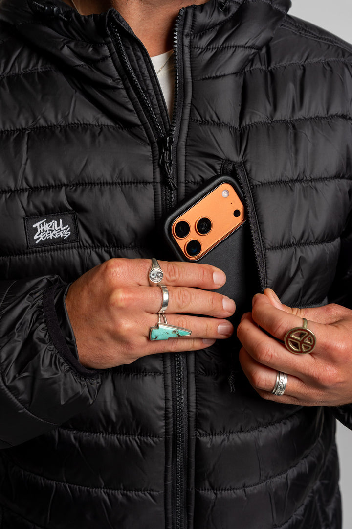 Person wearing a black puffer jacket putting a phone into the left chest pocket.