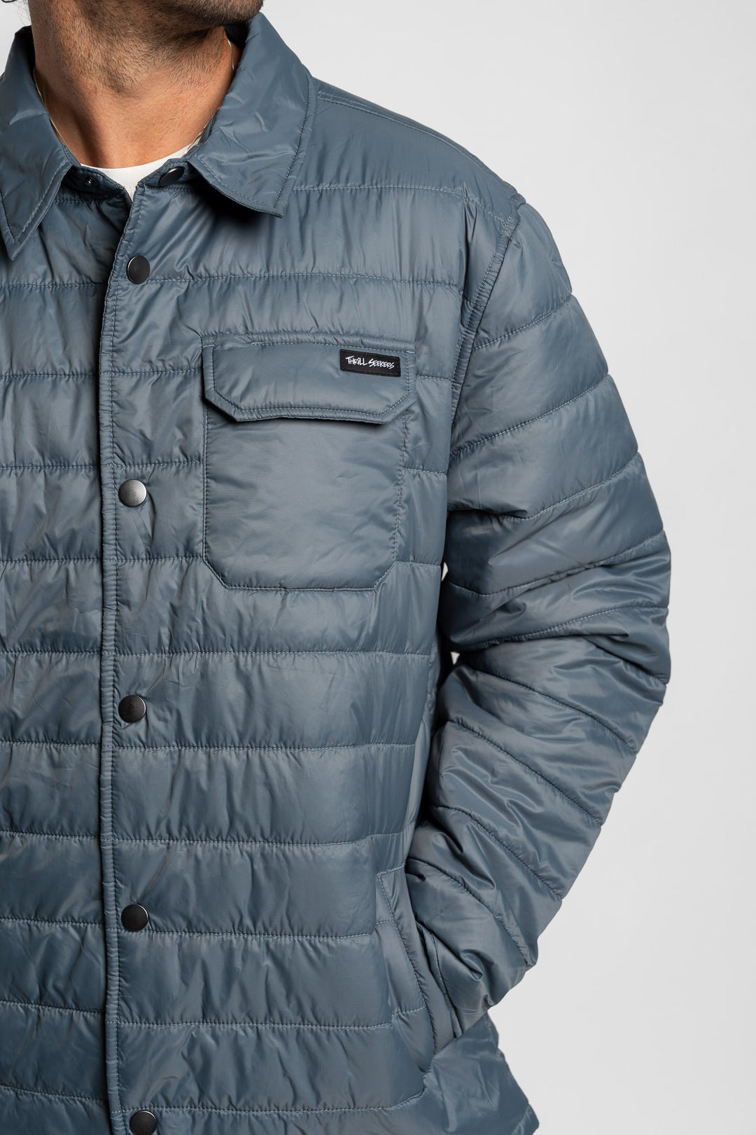 Blue quilted jacket with a Thrill Seekers logo on a white background
