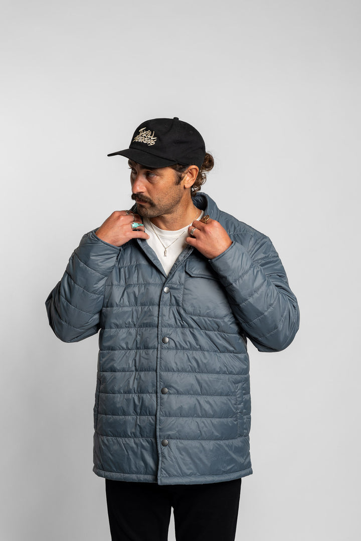 Man wearing a blue puffer jacket and black cap on a light gray background