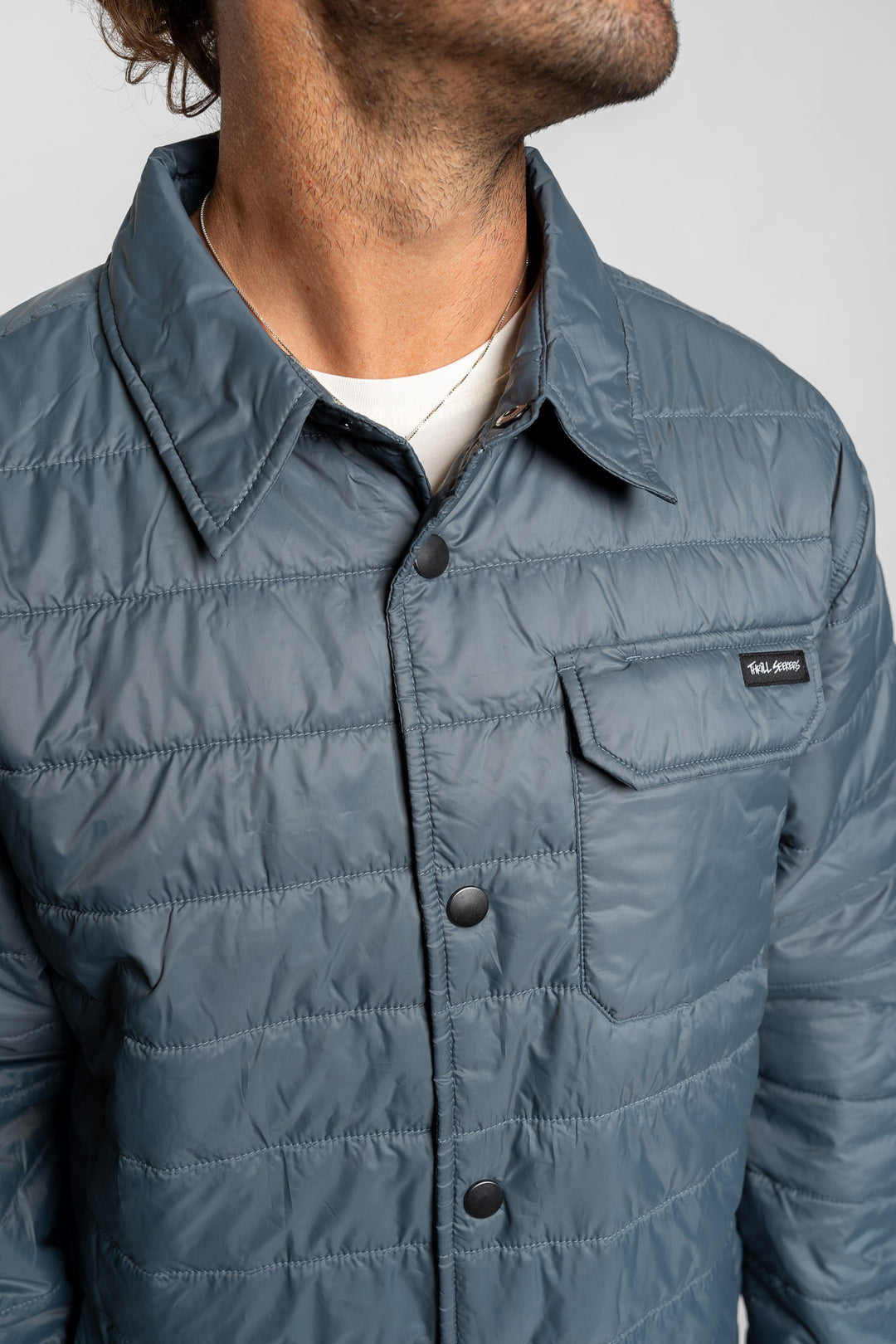 Close-up of a person wearing a blue quilted jacket with a Thrill Seekers logo.