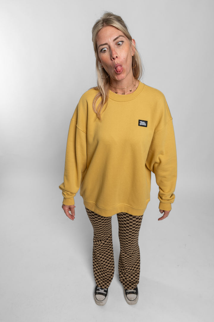 Person wearing a mustard yellow sweatshirt with a small logo on a plain background