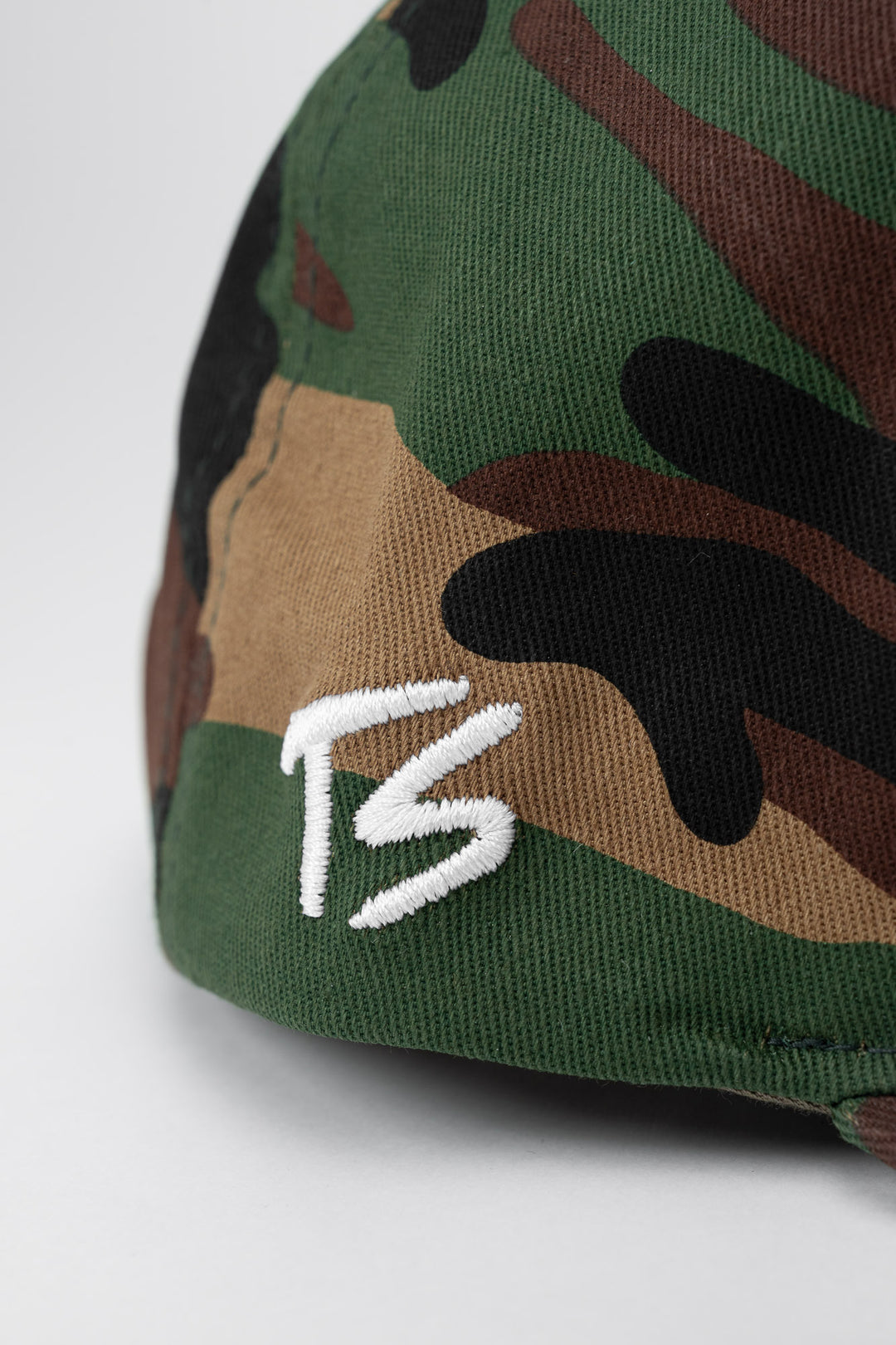 Camouflage cap with white embroidered 'ts' logo on a white background