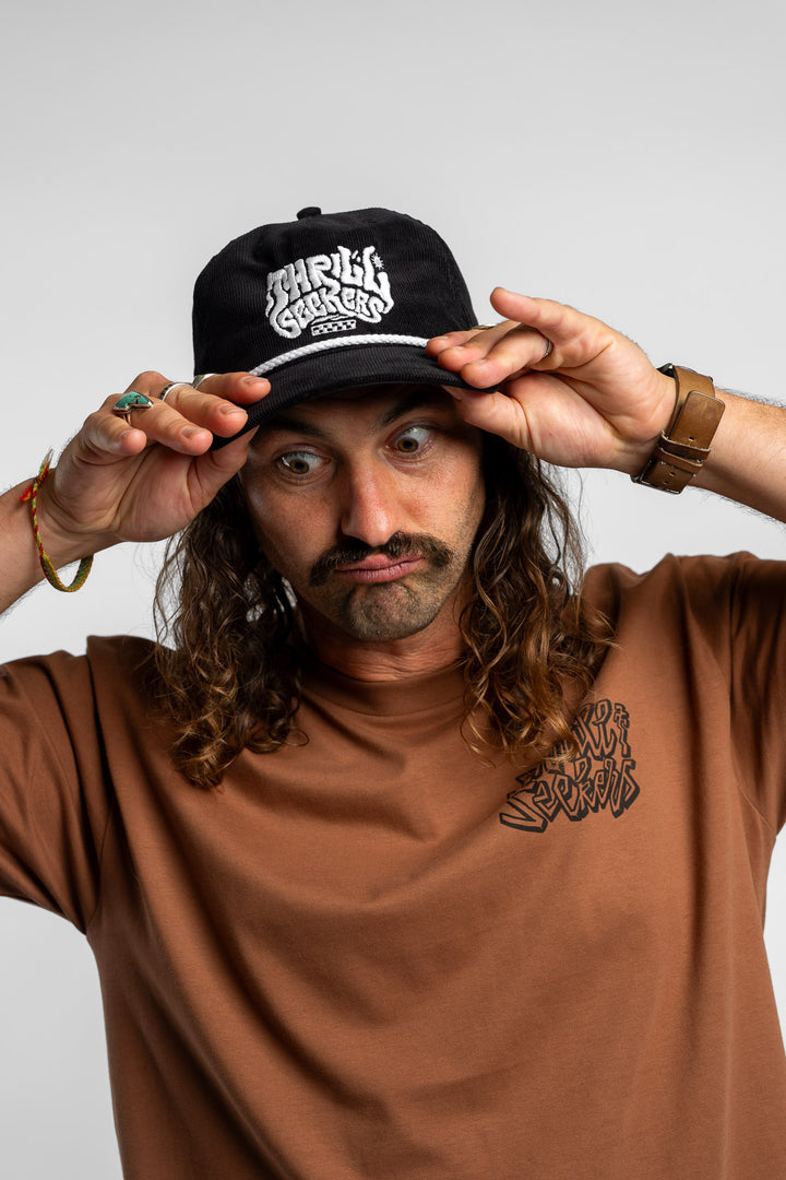 Person wearing a black corduroy cap with 'Thrill Seekers' logo on a white background