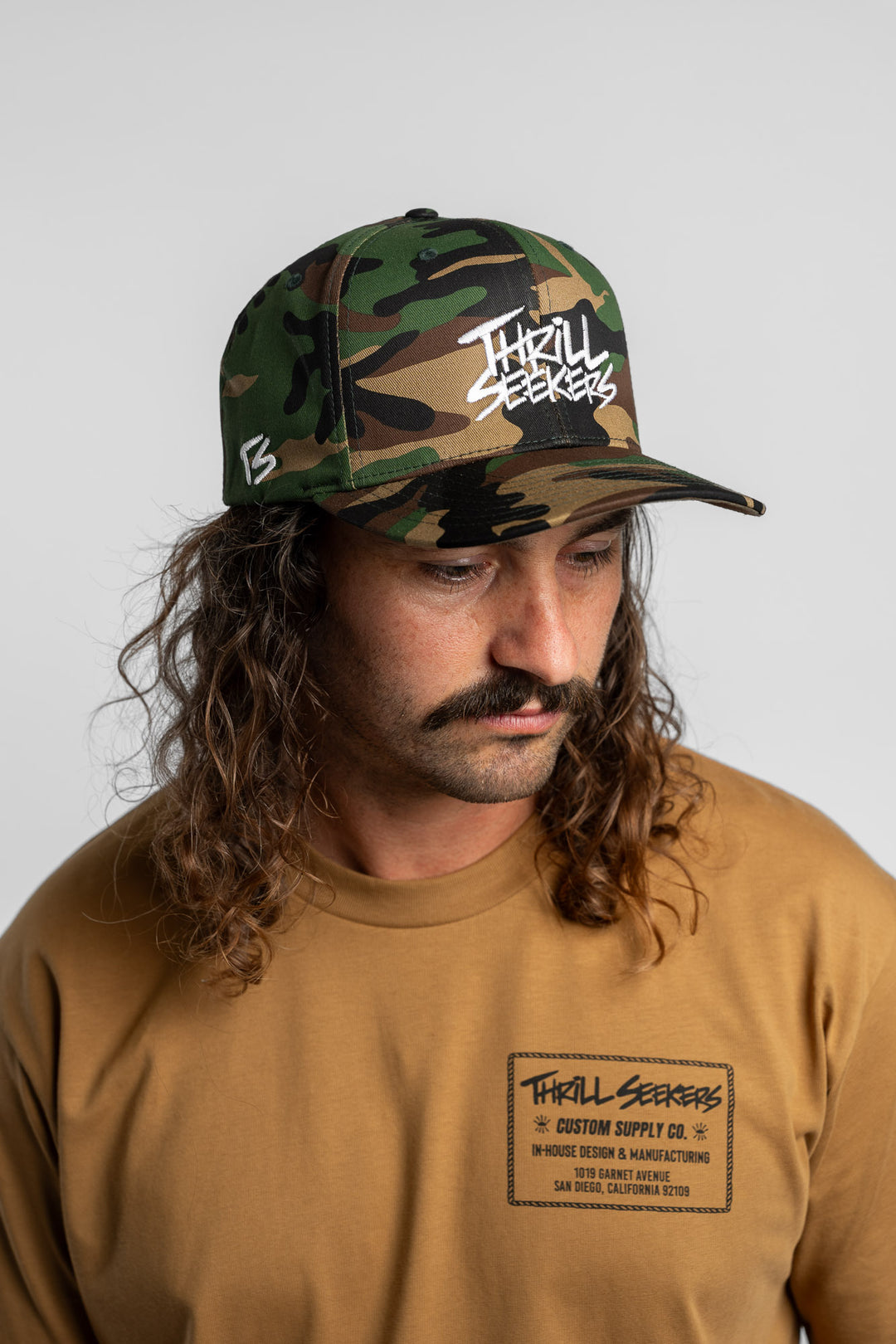 Person wearing a camo snapback hat with 'Thrill Seekers' logo in white
