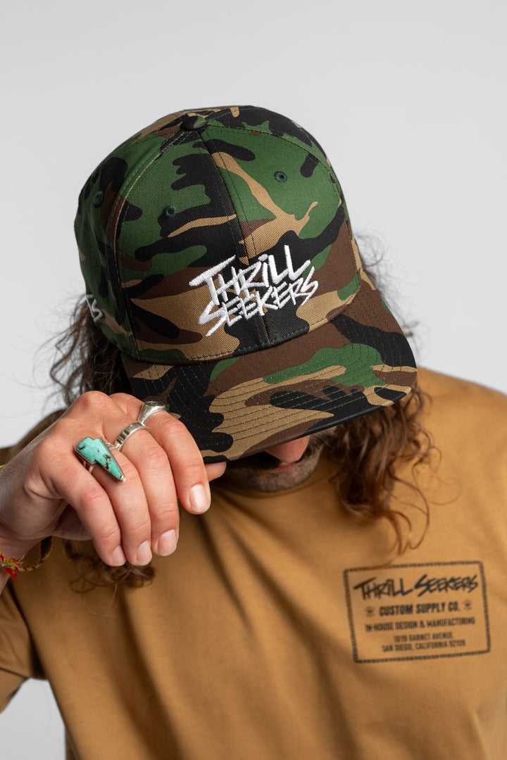 Person wearing a camo snapback hat with 'Thrill Seekers' logo in white