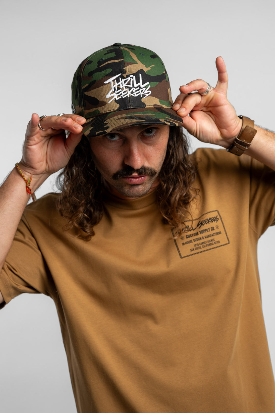 Person wearing a camo snapback hat with 'Thrill Seekers' logo in white