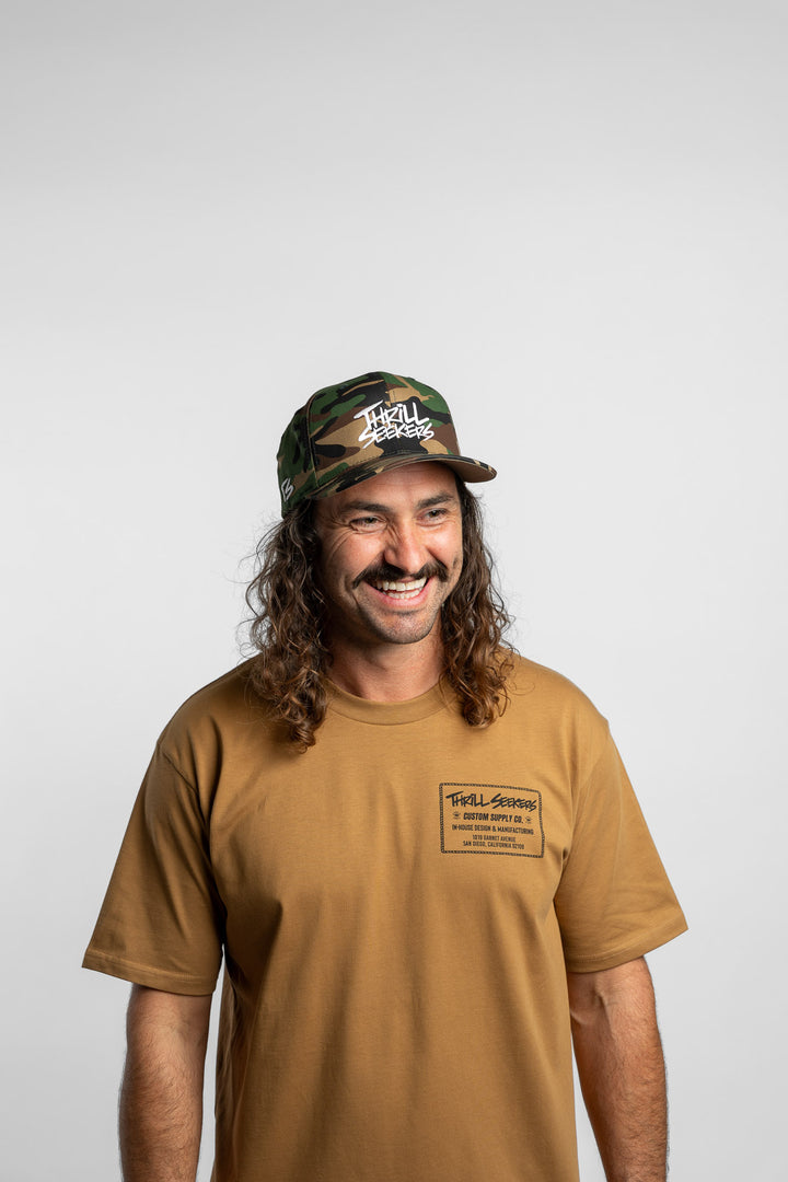 Person wearing a camo snapback hat with 'Thrill Seekers' logo in white
