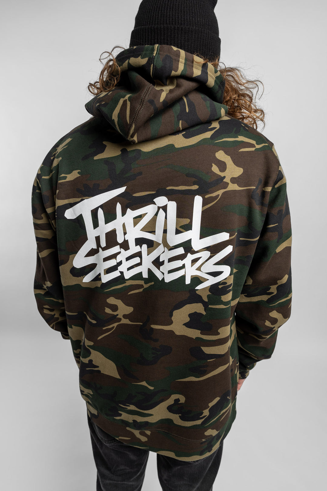 Person wearing camo hoodie with 'Thrill Seekers' logo in white