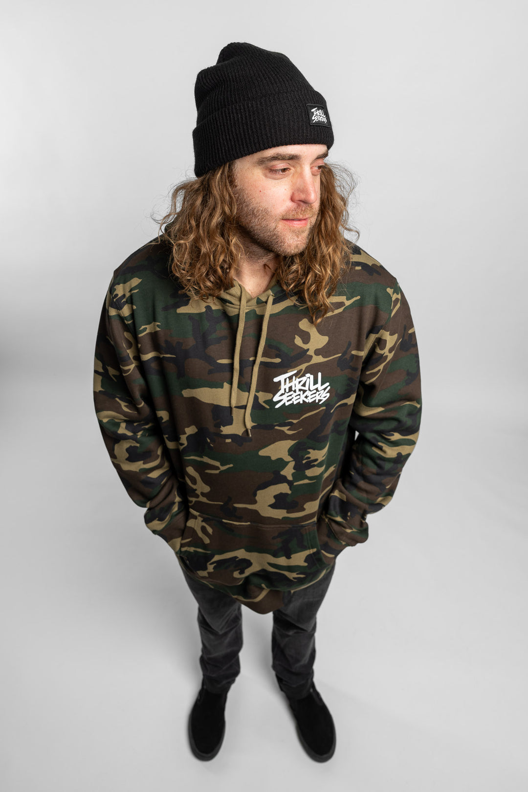 Person wearing camo hoodie with 'Thrill Seekers' logo in white