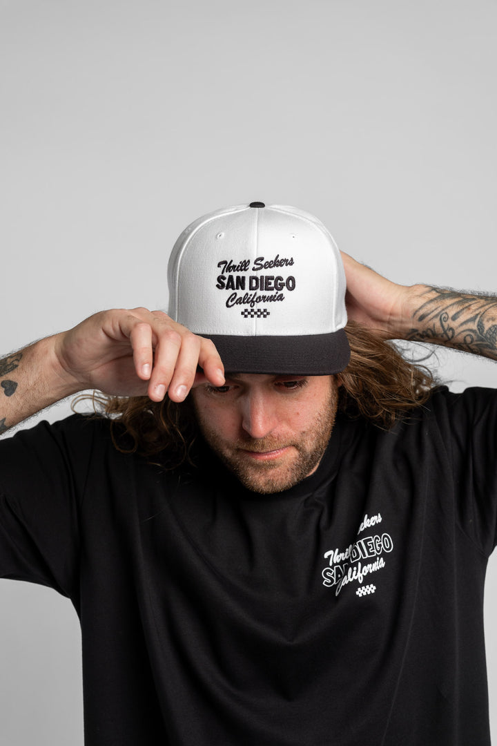 Person wearing a white and black snapback with 'Thrill Seekers' logo in black
