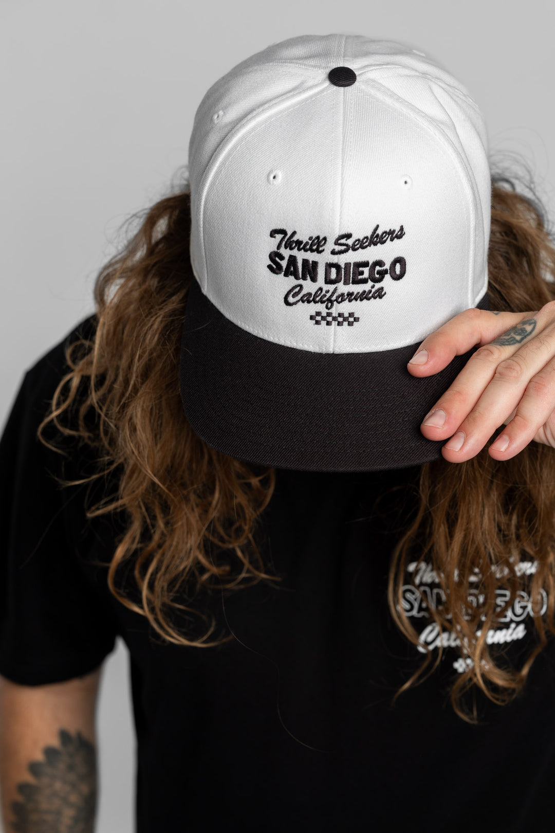 Person wearing a white and black snapback with 'Thrill Seekers' logo in black