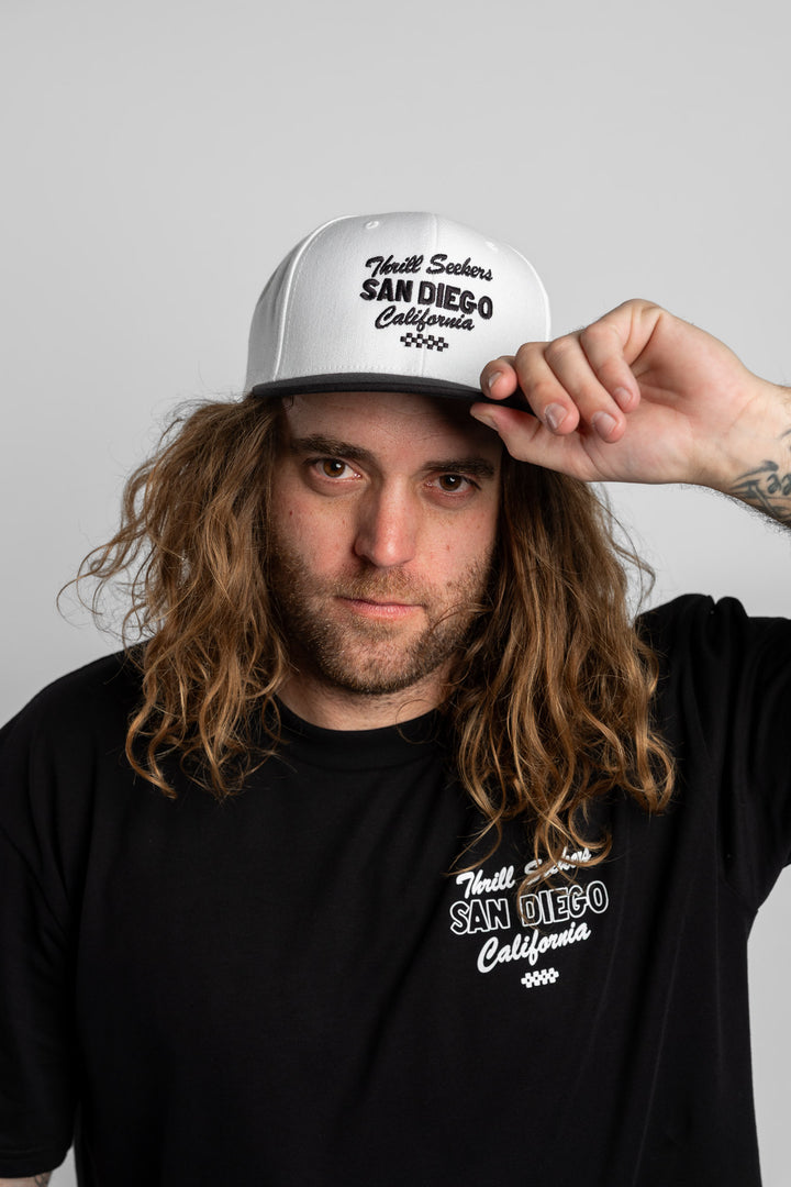 Person wearing a white and black snapback with 'Thrill Seekers' logo in black