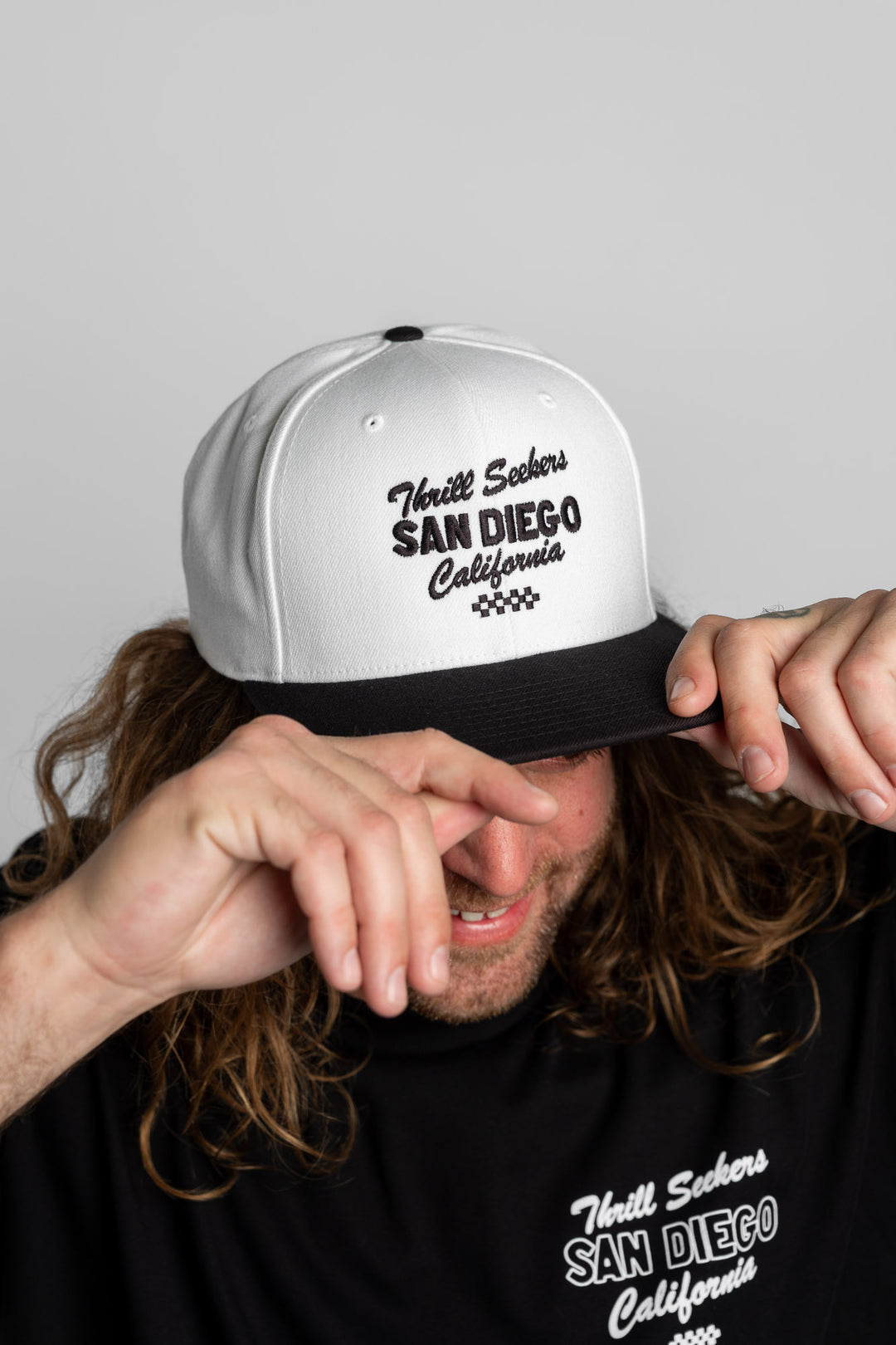 Person wearing a white and black snapback with 'Thrill Seekers' logo in black