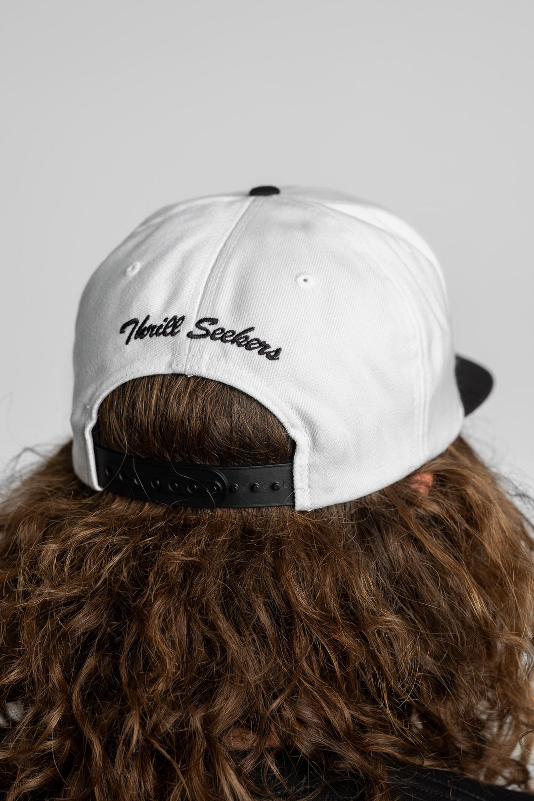 Person wearing a white and black snapback with 'Thrill Seekers' logo in black