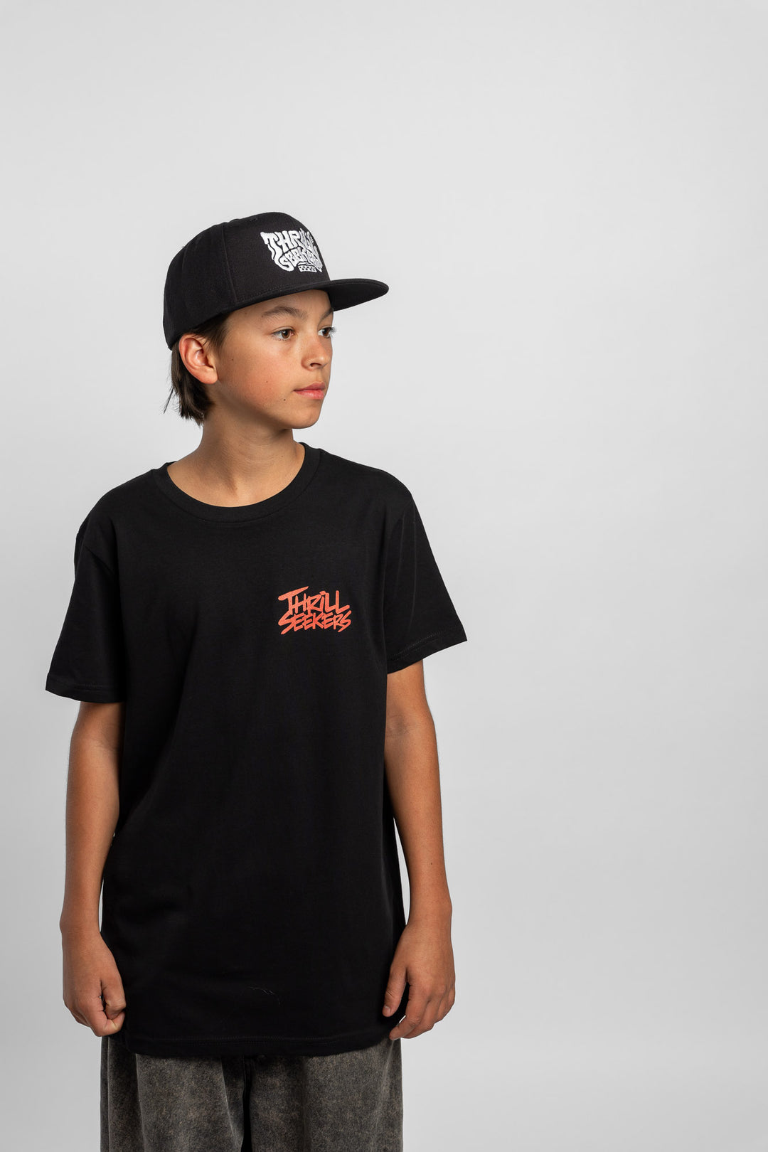 Kid wearing a black tee with 'Thrill Seekers' logo in cardinal red
