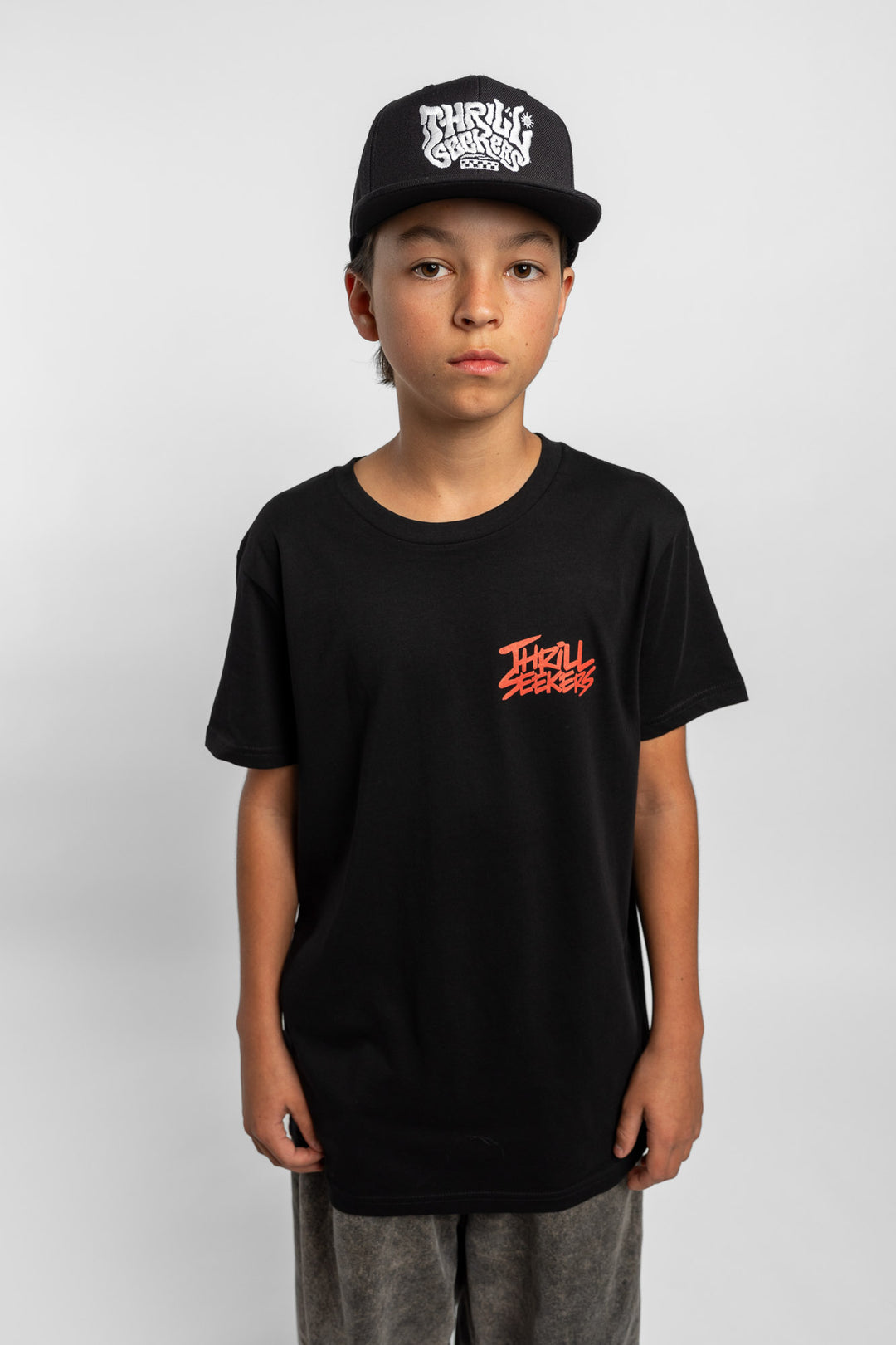Kid wearing a black tee with 'Thrill Seekers' logo in cardinal red