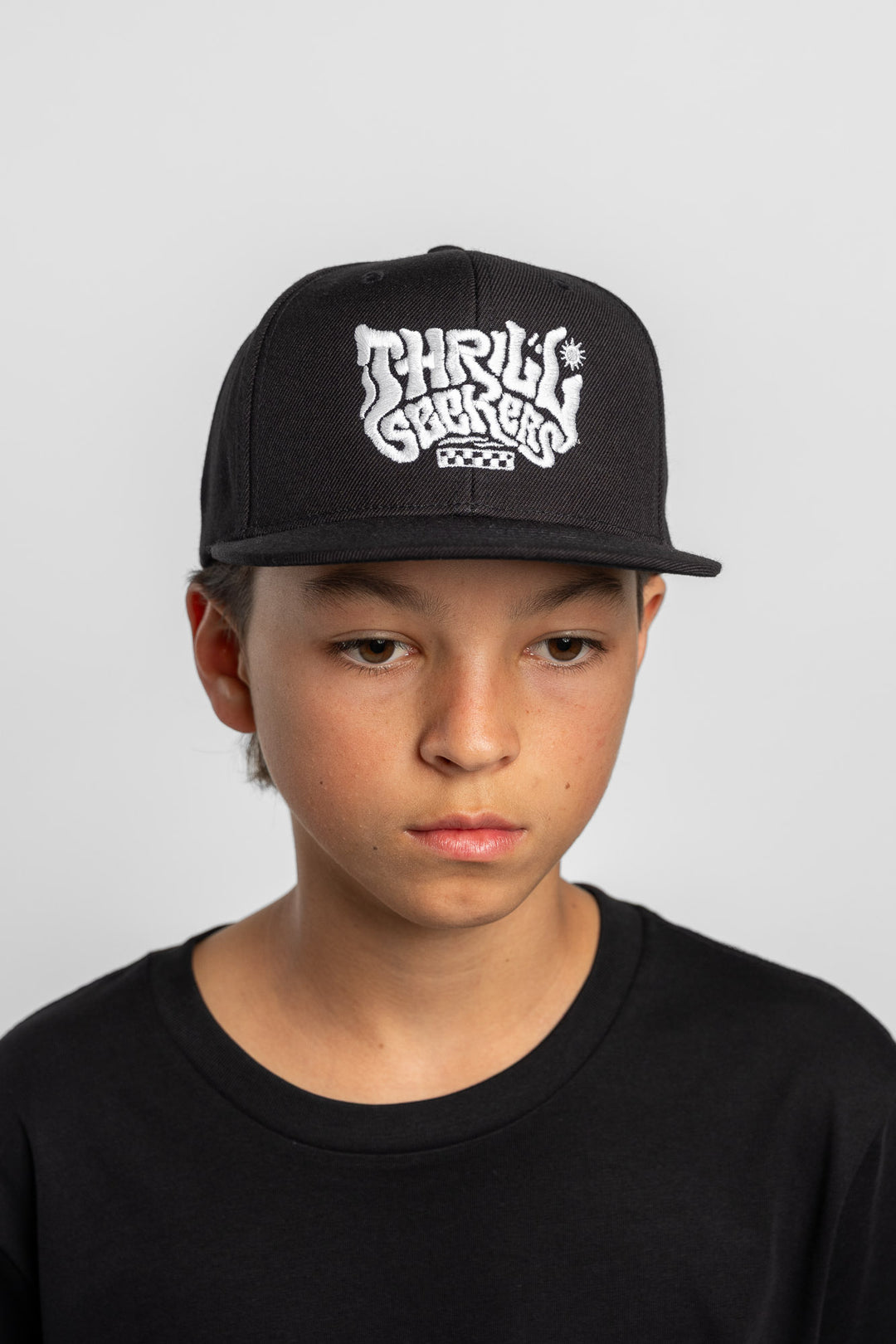 Person wearing a black cap with 'Thrill Seekers' logo on a white background