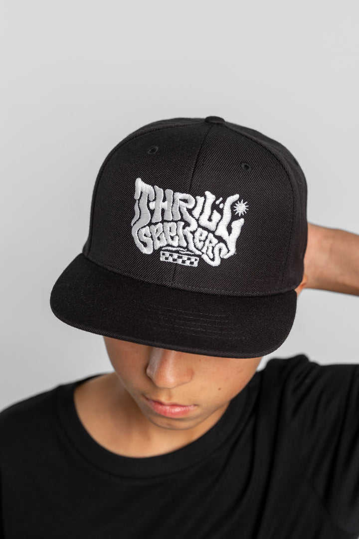 Person wearing a black cap with 'Thrill Seekers' logo on a white background