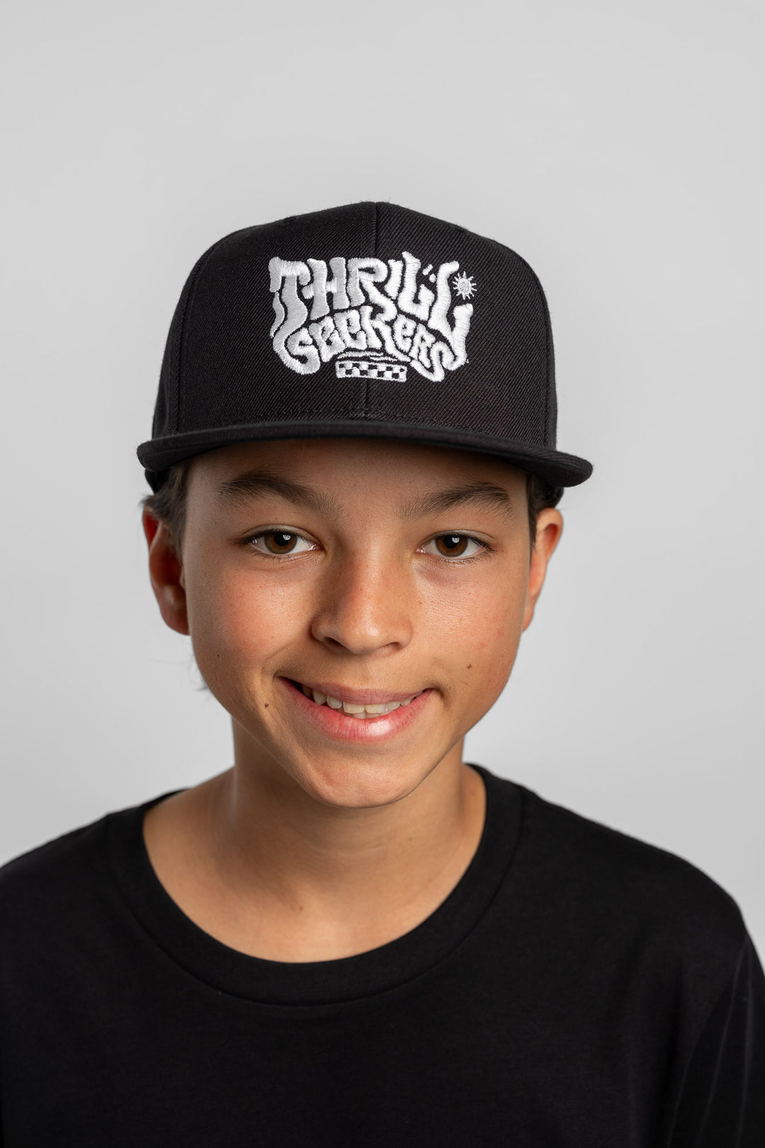 Person wearing a black cap with 'Thrill Seekers' logo on a white background