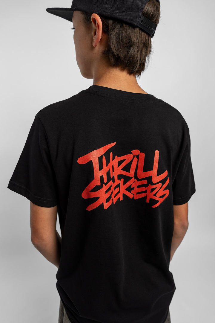 Kid wearing a black tee with 'Thrill Seekers' logo in cardinal red