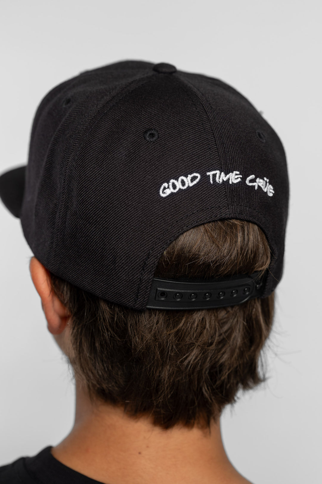 Back of a black cap with 'Good Time Crue' text on a person with a white background