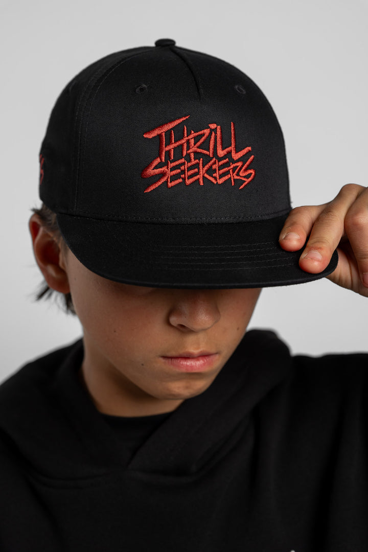 Person wearing a black cap with cardinal red 'Thrill Seekers' text on a white background