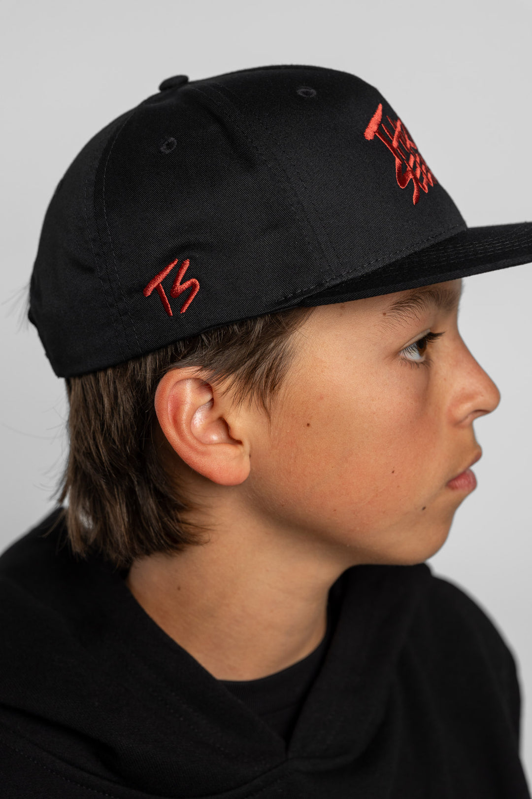 Side profile of a kid wearing a hat featuring an embroidered 'ts' logo in cardinal red