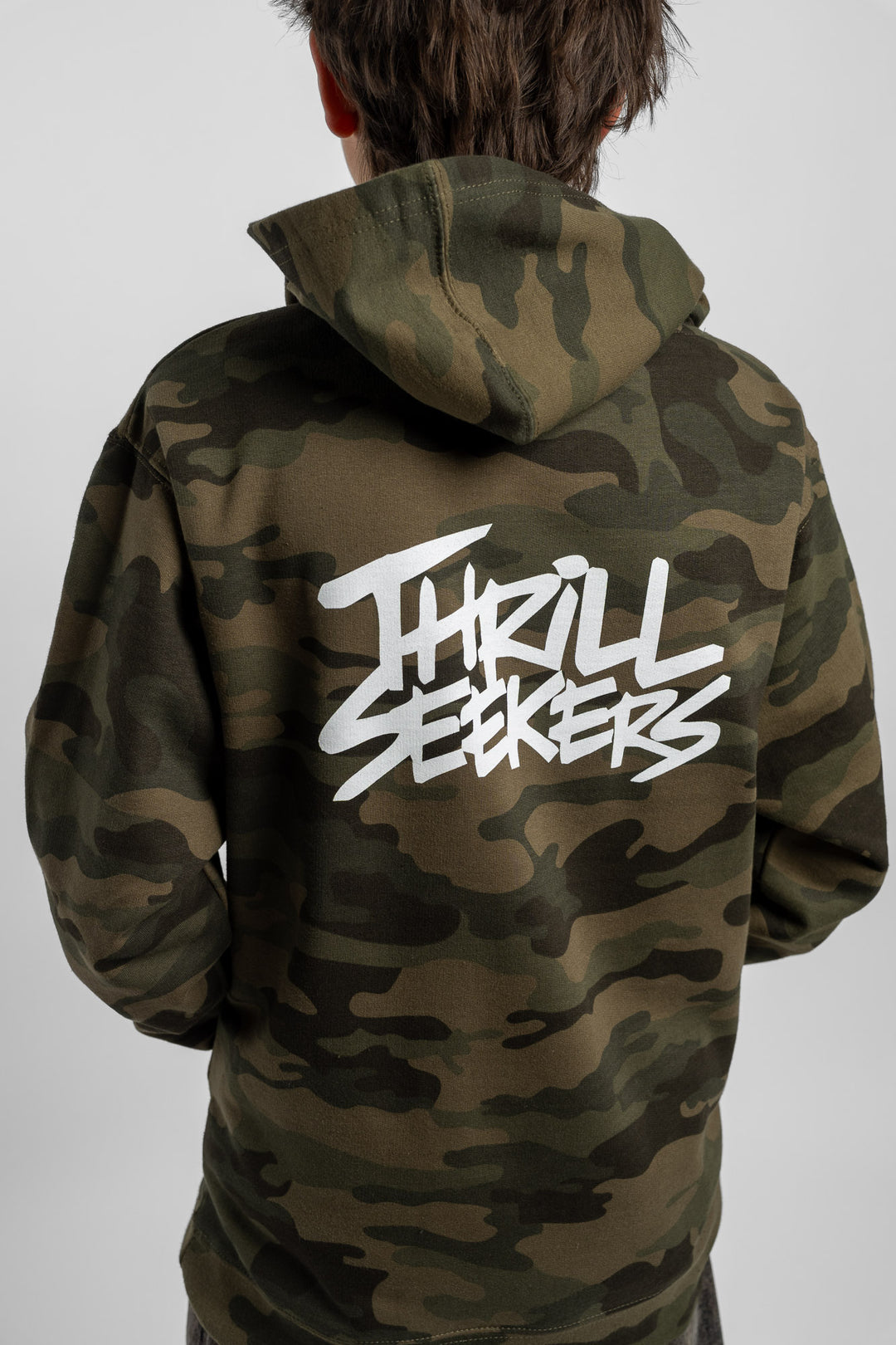 Kid wearing a camo hoodie with 'Thrill Seekers' logo in white