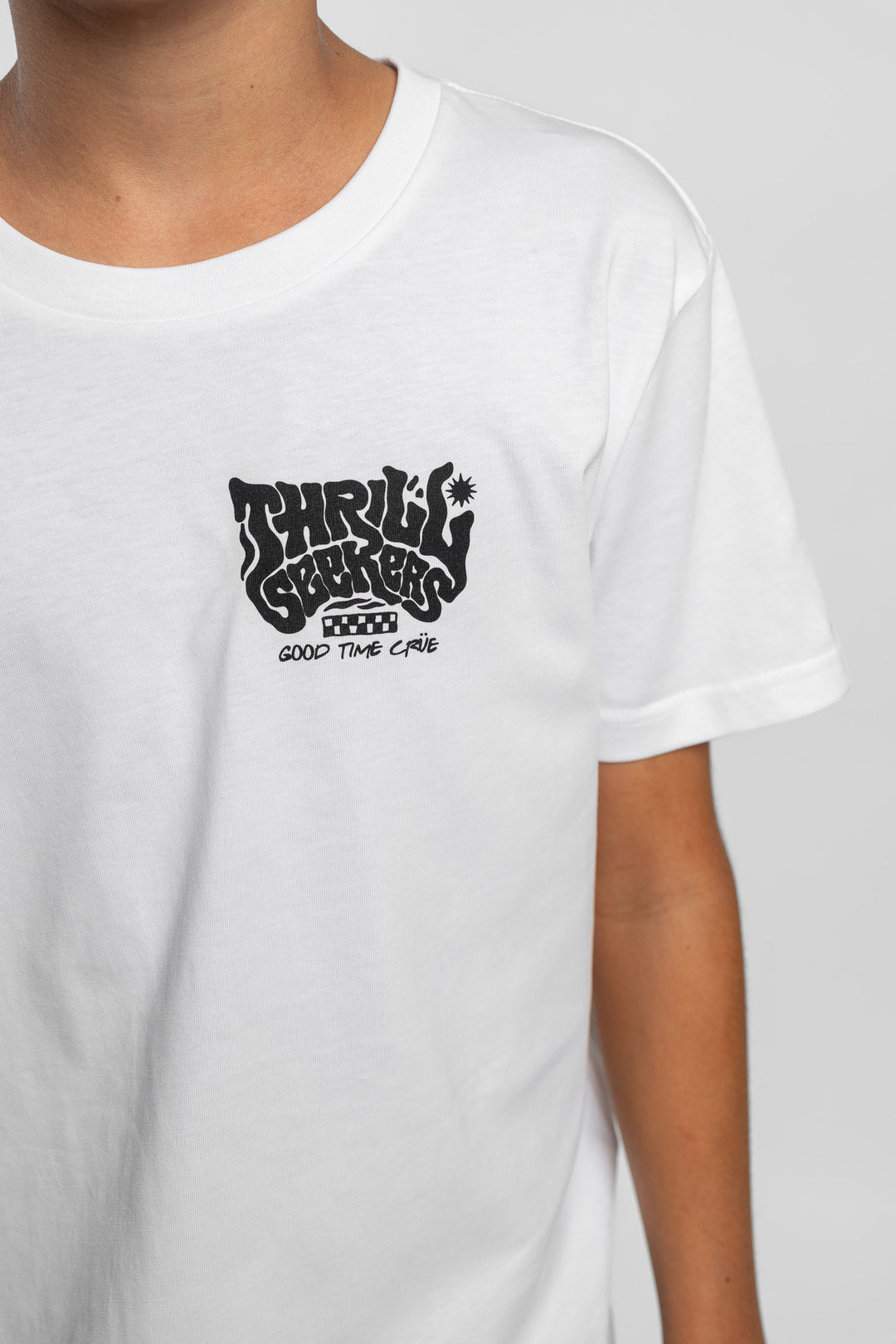 Kid wearing a white tee with 'Thrill Seekers' smokin logo in black