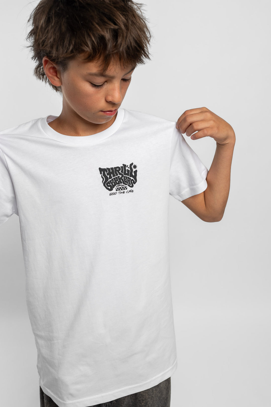 Kid wearing a white tee with 'Thrill Seekers' smokin logo in black