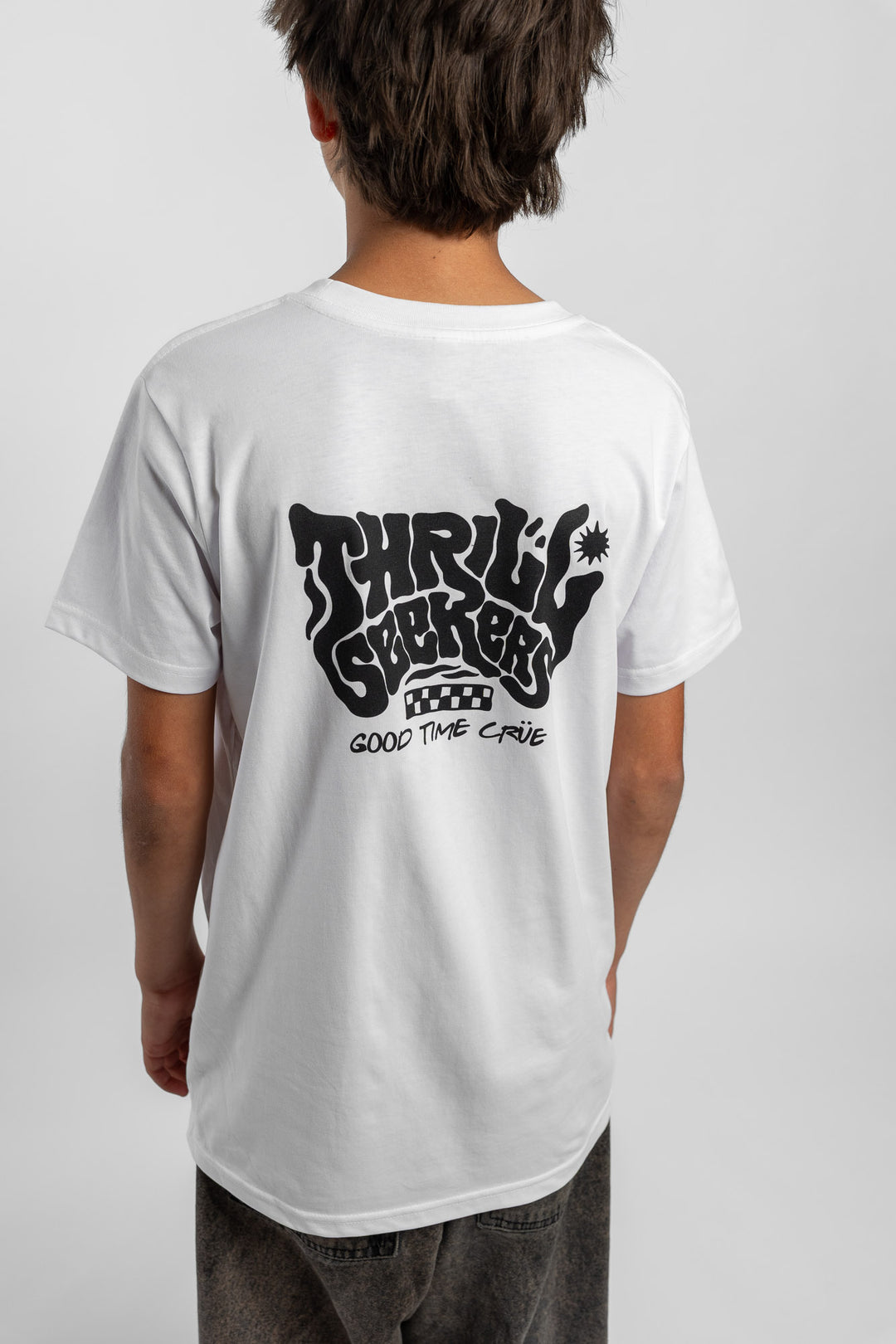 Kid wearing a white tee with 'Thrill Seekers' smokin logo in black