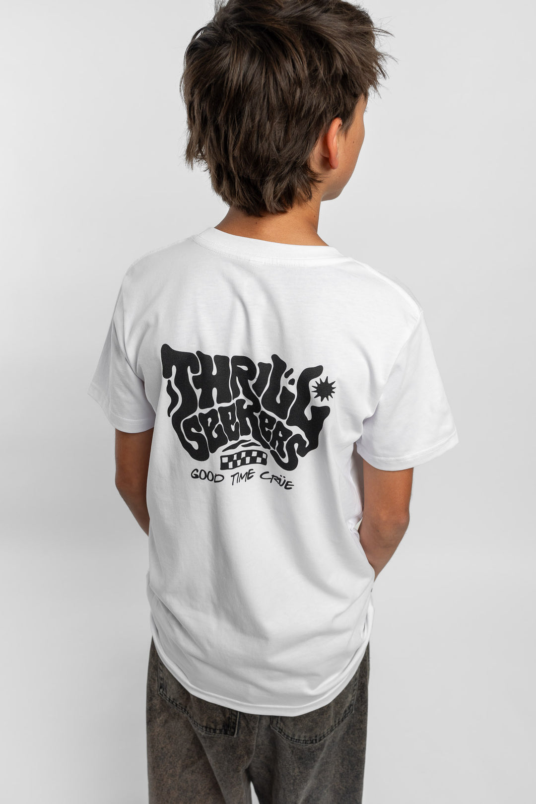 Kid wearing a white tee with 'Thrill Seekers' smokin logo in black