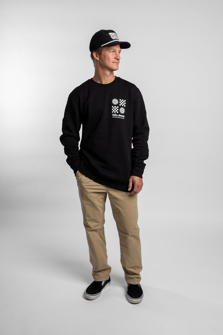Person wearing a black crewneck with a 'Thrill Seekers' tile logo