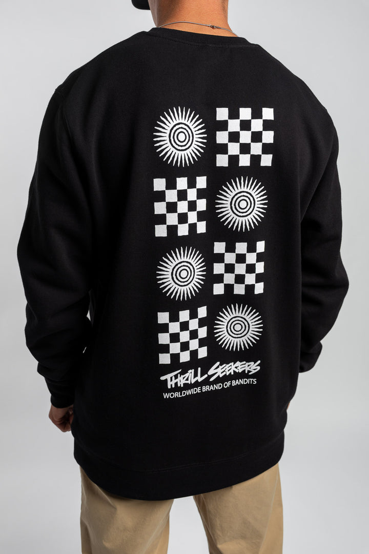 Person wearing a black crewneck with a 'Thrill Seekers' tile logo