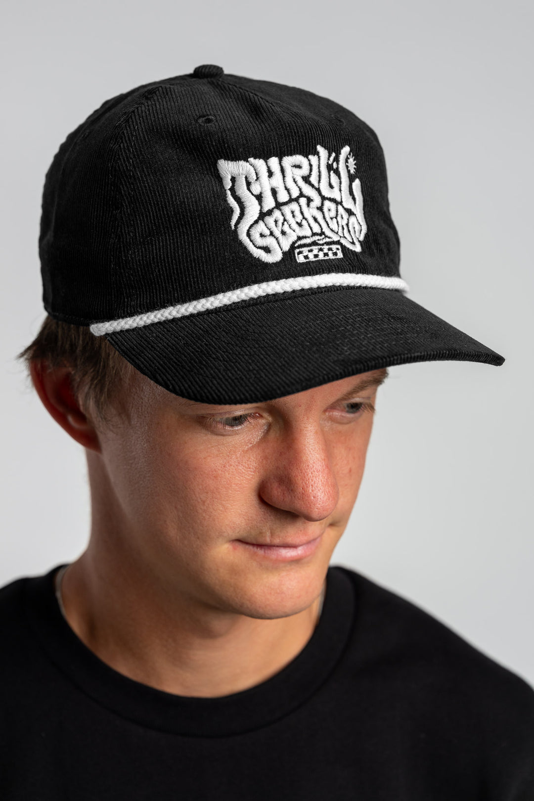 Person wearing a black corduroy cap with 'Thrill Seekers' logo on a white background
