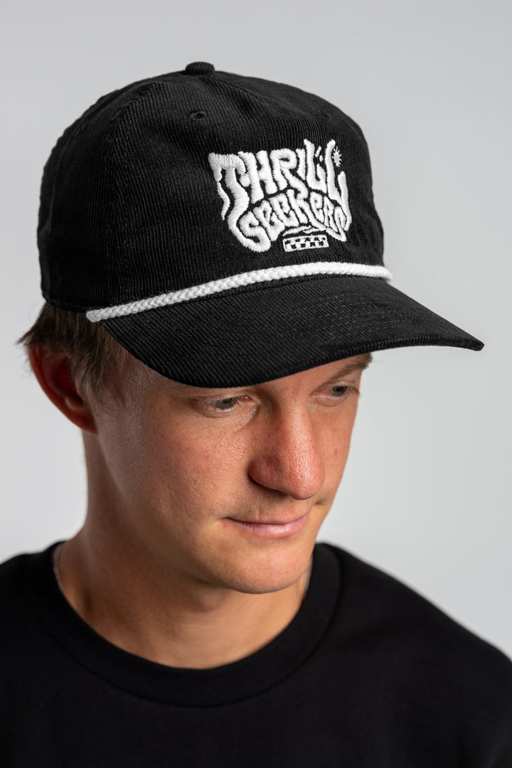 Person wearing a black corduroy cap with 'Thrill Seekers' logo on a white background