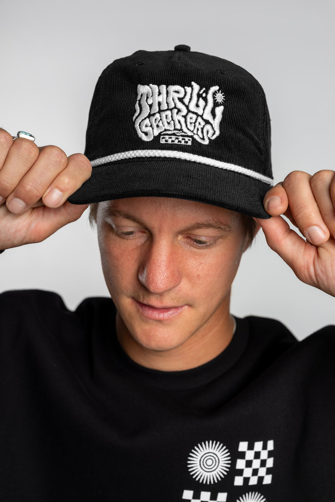 Person wearing a black corduroy cap with 'Thrill Seekers' logo on a white background