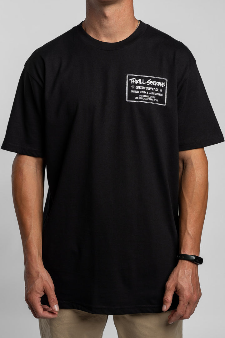 Person wearing black tee with 'Thrill Seekers' workman logo in white