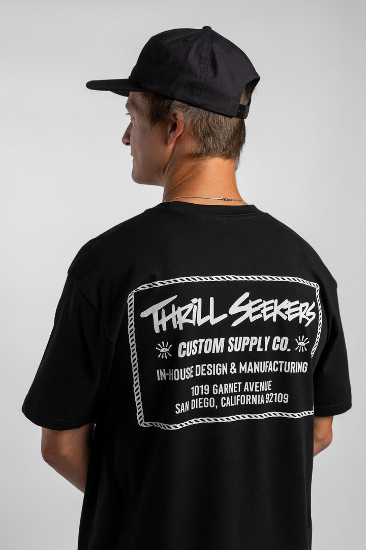 Person wearing black tee with 'Thrill Seekers' workman logo in white