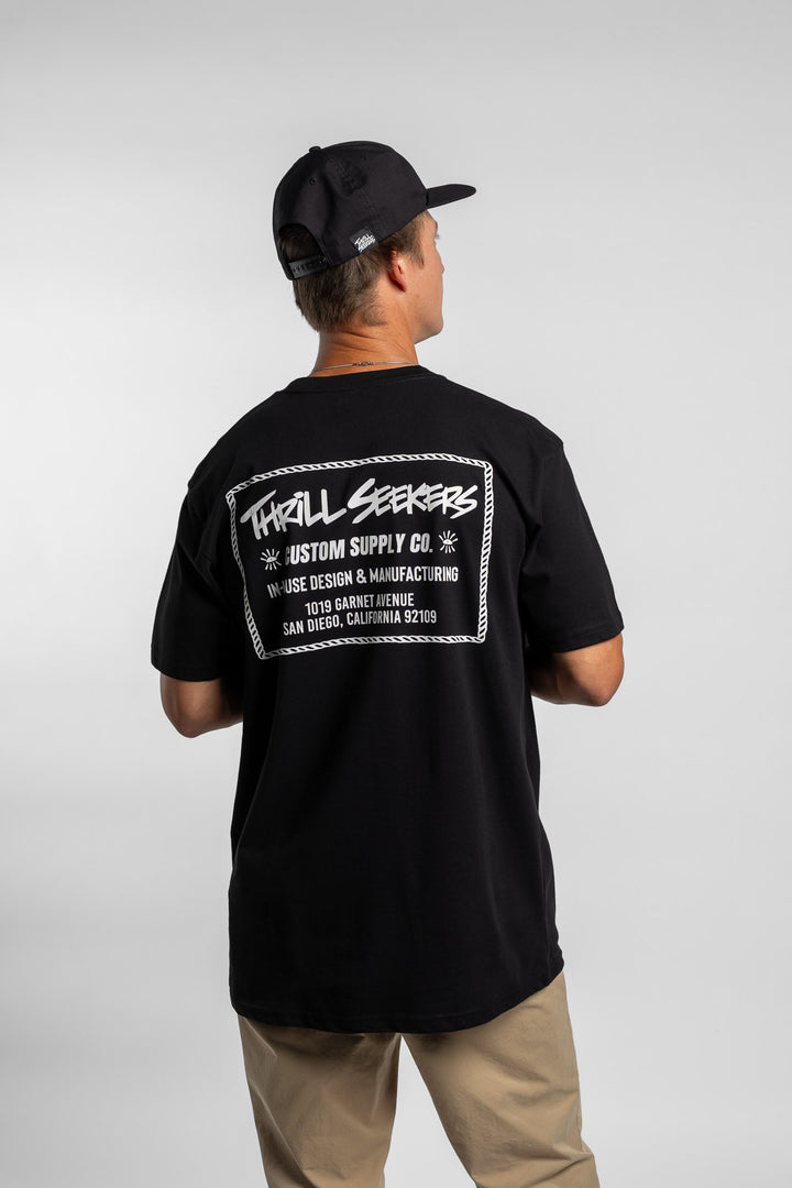 Person wearing black tee with 'Thrill Seekers' workman logo in white