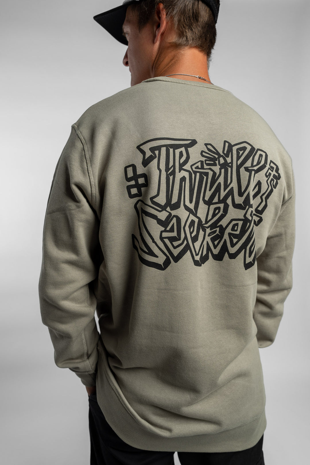 Person wearing eucalyptus crewneck with 'Thrill Seekers' scribe logo
