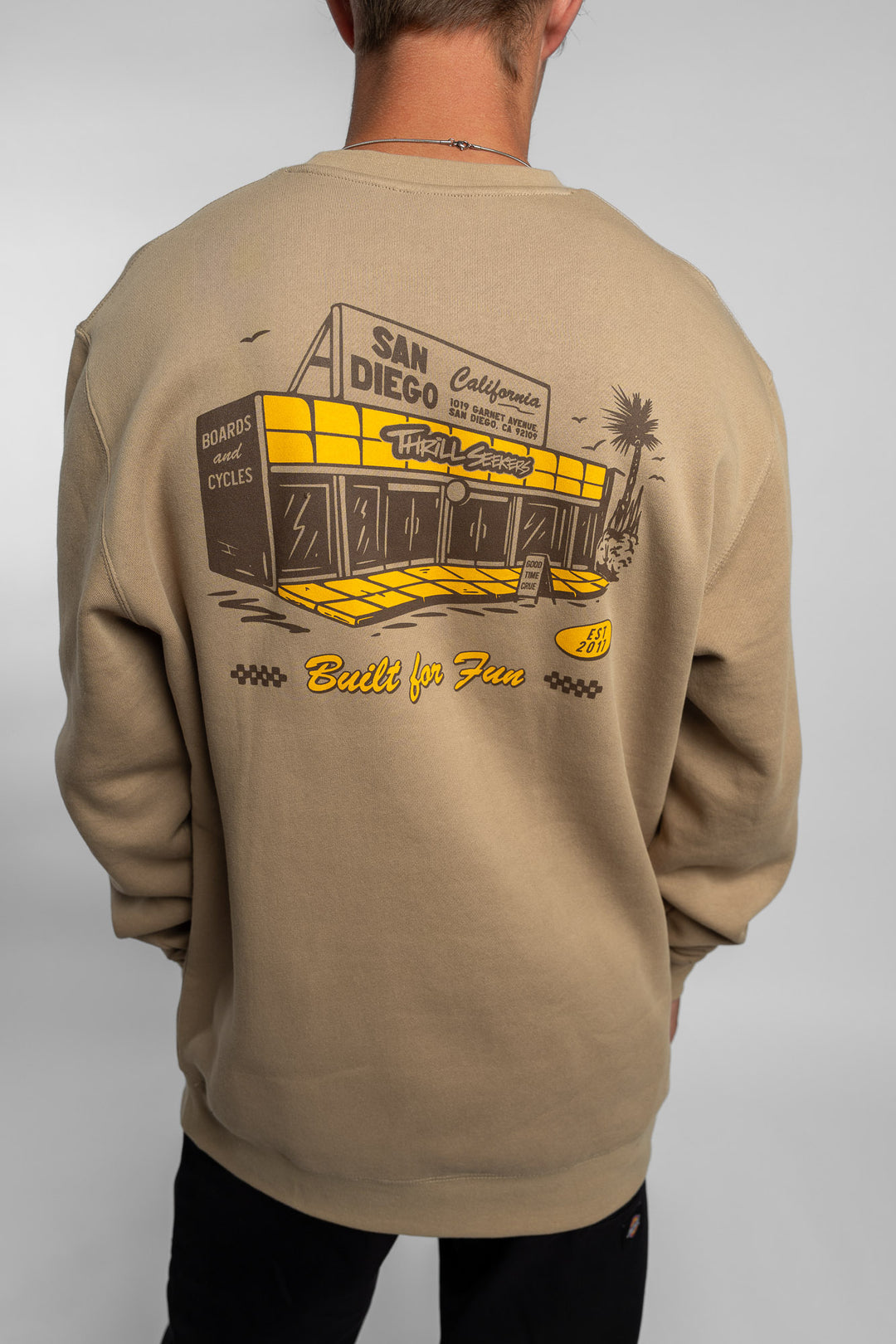 Person wearing sand crewneck with 'Thrill Seekers' shop logo