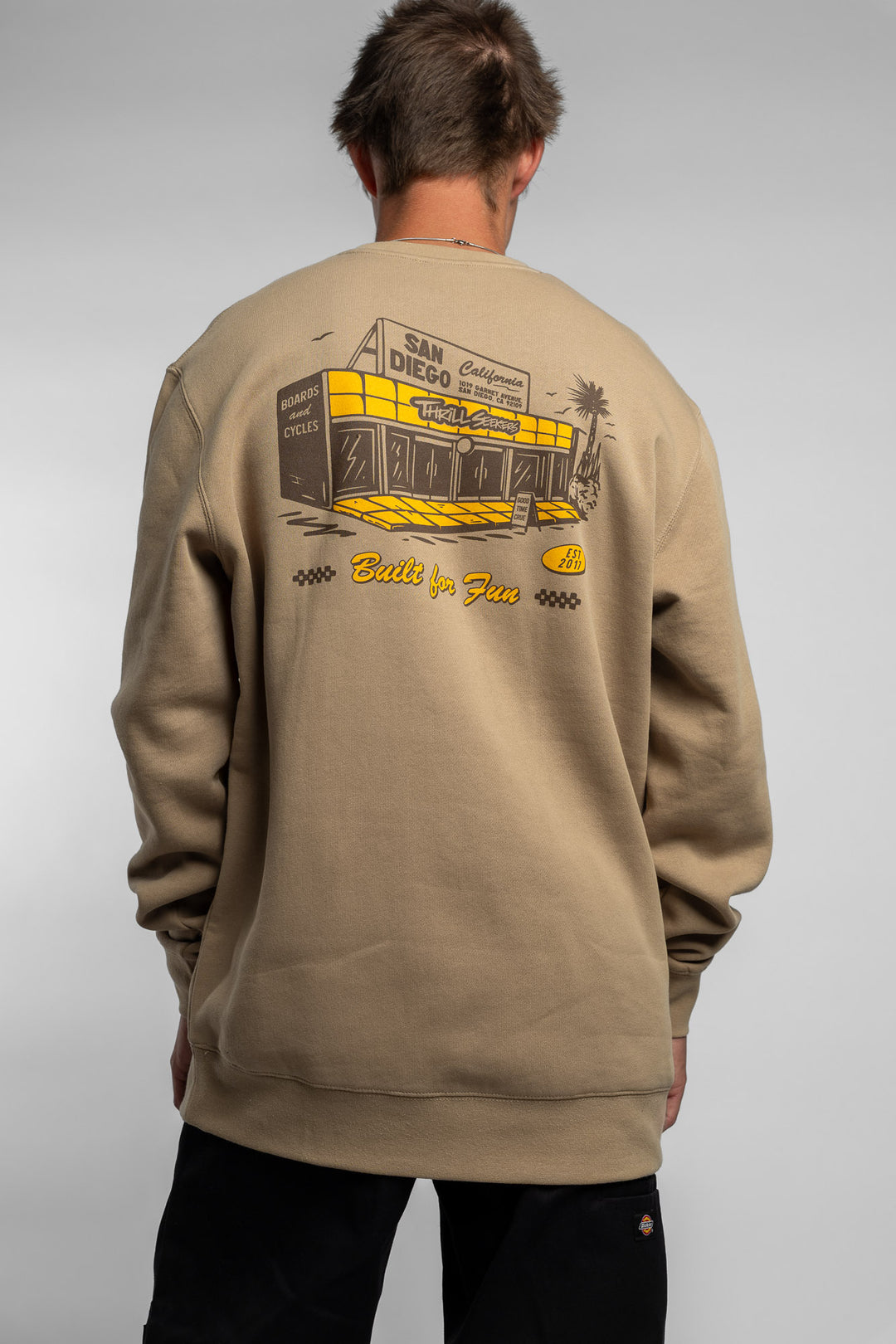 Person wearing sand crewneck with 'Thrill Seekers' shop logo
