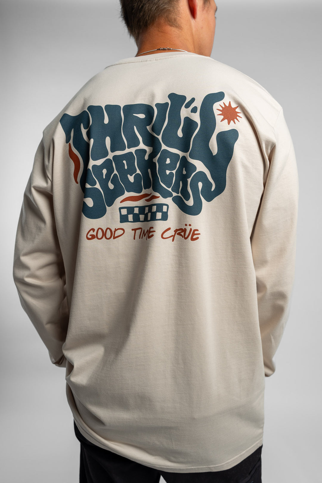 Person wearing a bone colored long-sleeve shirt with a 'Thrill Seekers' logo