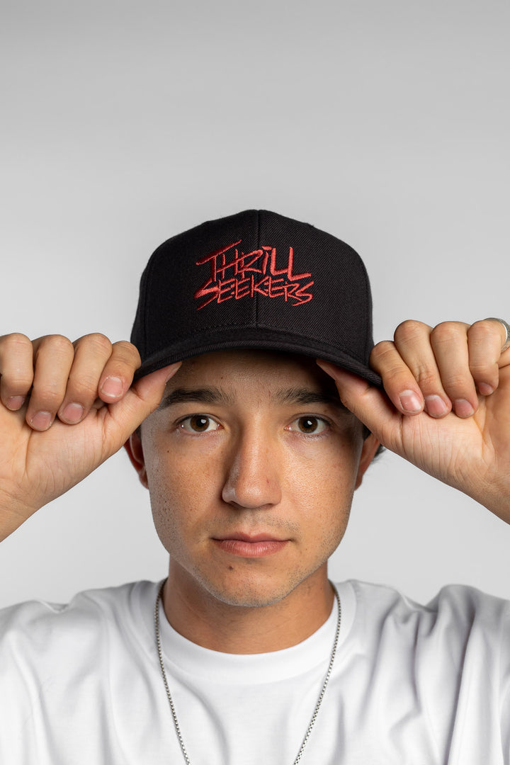 Person in black snapback hat with 'Thrill Seekers' logo in cardinal red